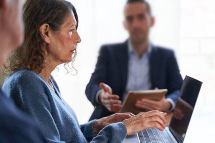 Old woman typing on laptop while man talks to her - Employment Law